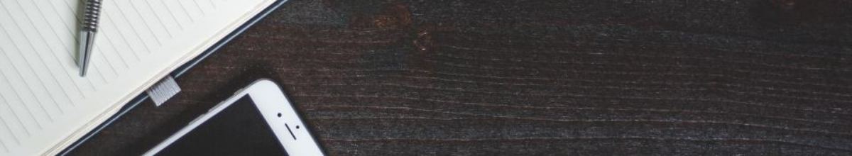 A notebook, a pen and a mobile telephone lying on a dark wooden desk.